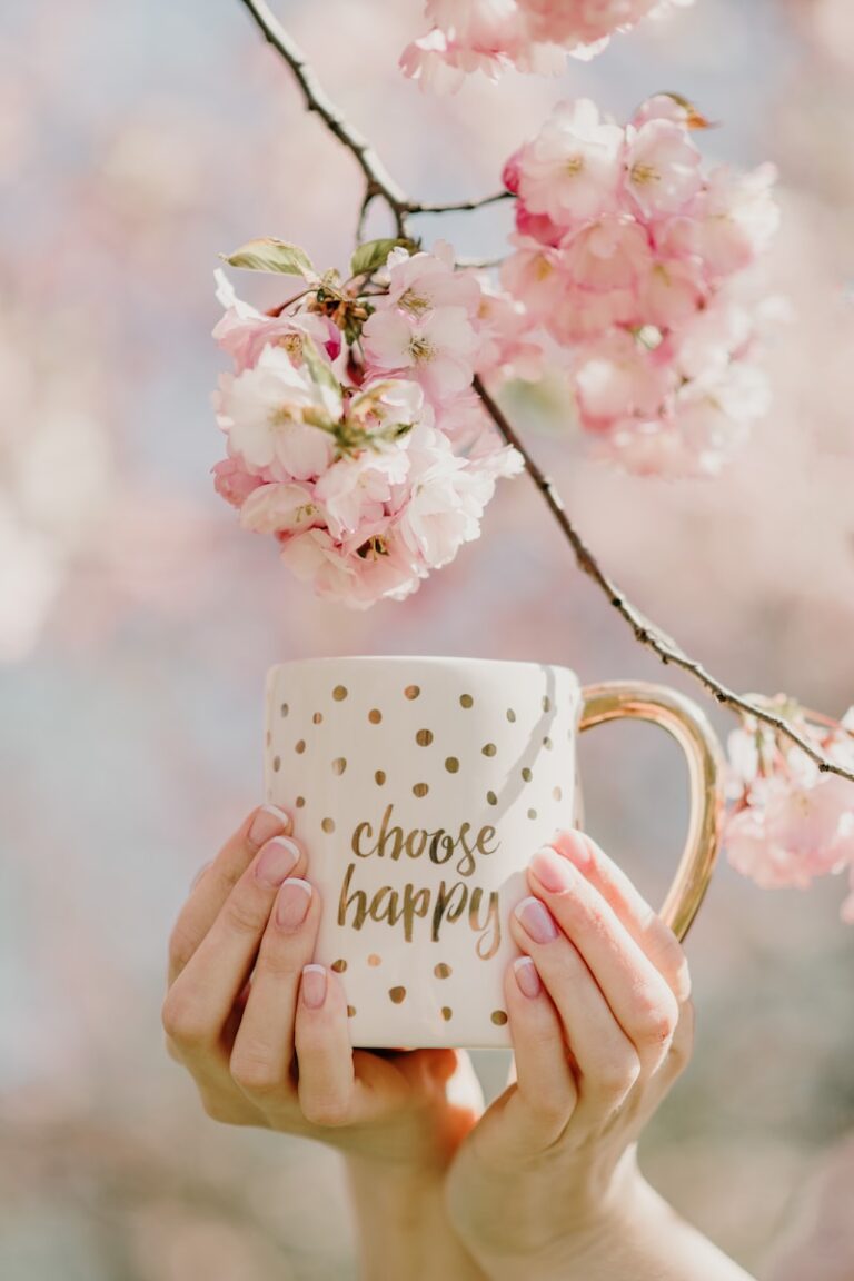 a woman holding a coffee mug with a cherry blossom tree in the background